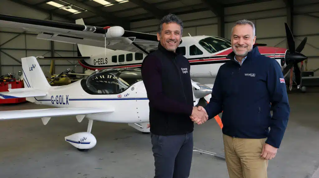 Nigel Church, CEO of Emerge Digital (left), and Nick Weston, CEO of Weston Aviation (right), shaking hands in an aircraft hangar, surrounded by aircraft.